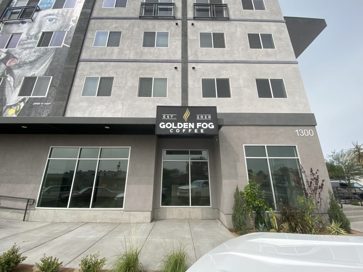 Exterior of Golden Fog Coffee Shop with a grey building and a black sign